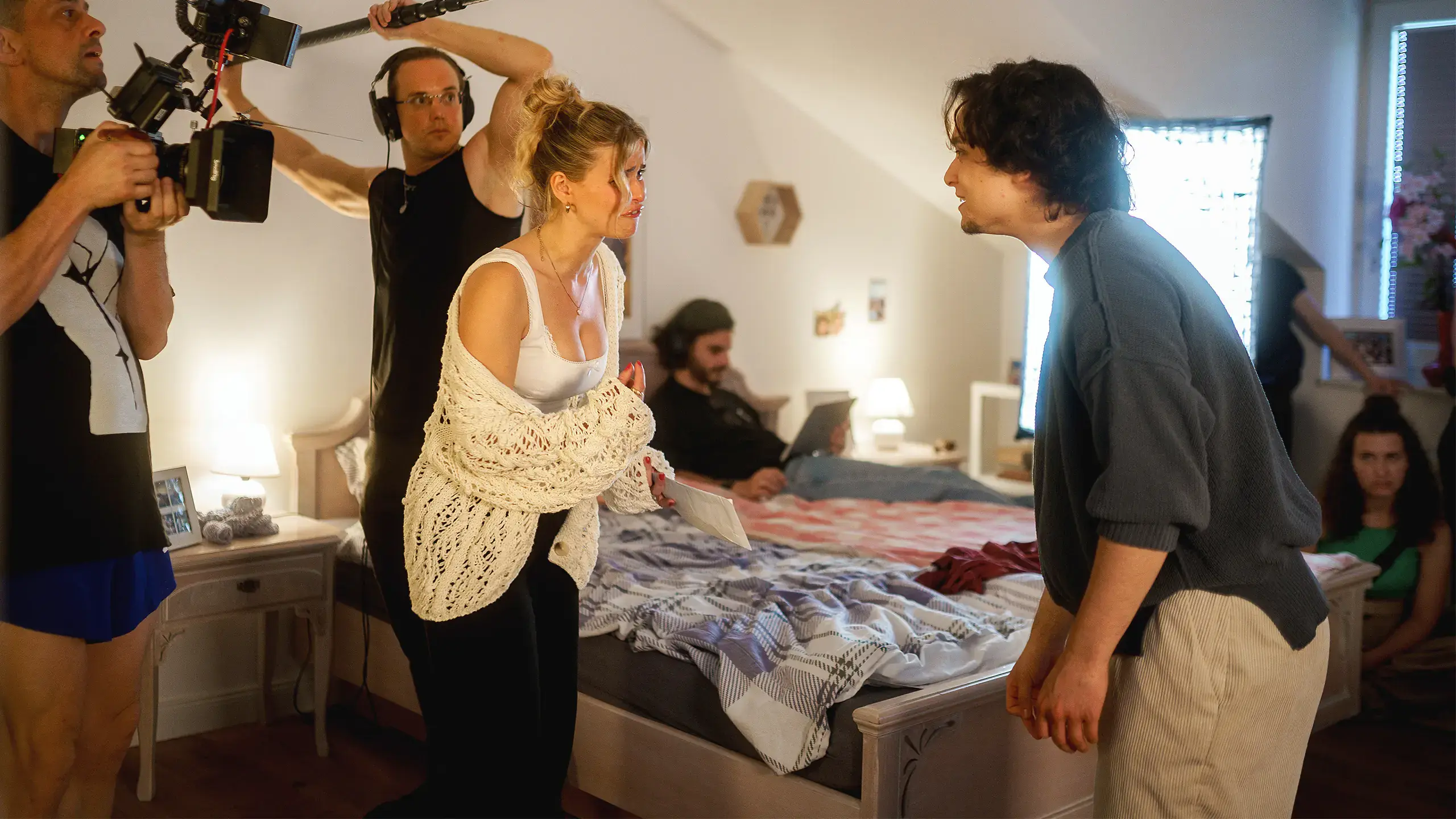 Filmcrew mit Kamera und Tonangel bei Dreharbeiten in einem Schlafzimmer-Set mit zwei Schauspielern